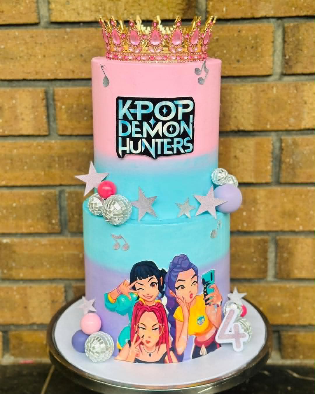 Two-tier K-Pop Demon Hunters birthday cake in pink, blue and purple with crown topper